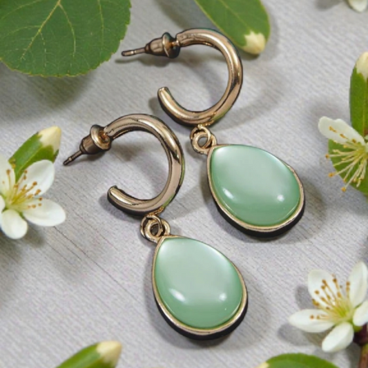Gold earrings with green teardrop stones on a floral background